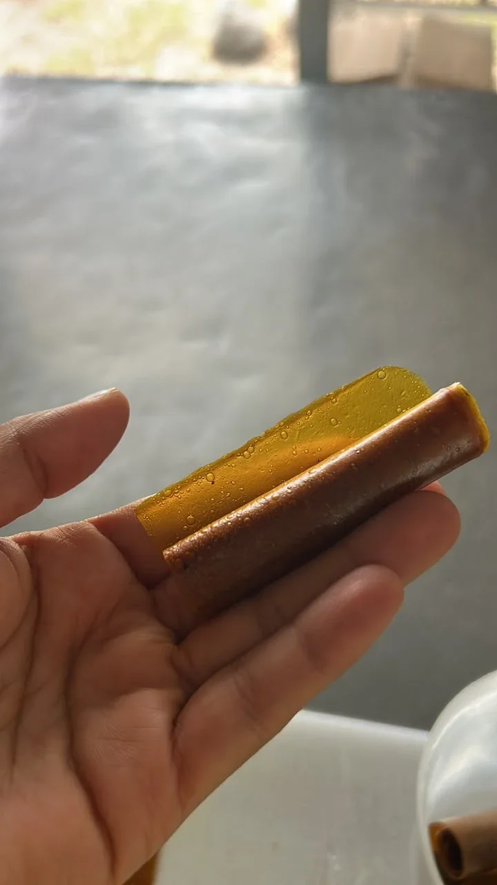 Mano sosteniendo un Roll-Up de fruta a medio desenrollar, mostrando la lámina flexible